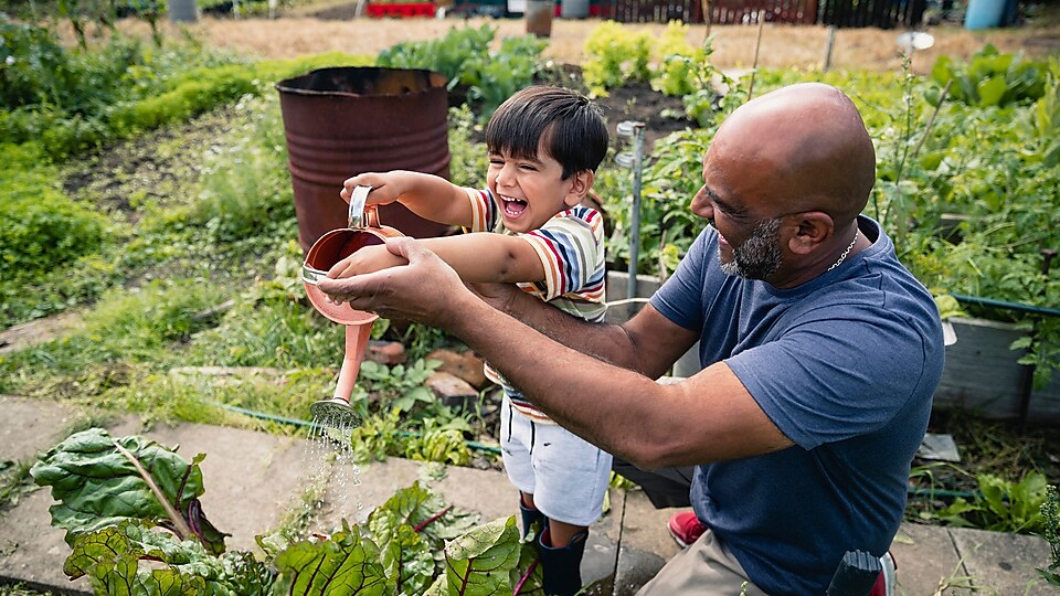 Gülen bir çocuğun bahçede çiçekleri sulamasına yardım eden adam