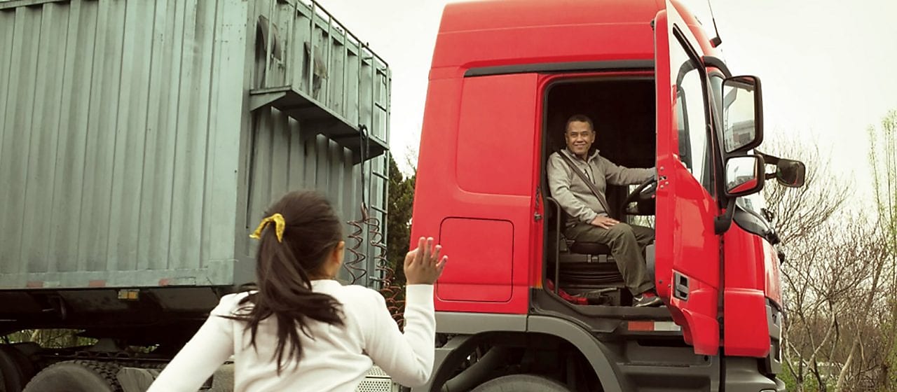 Kapısı açık kırmızı kamyondaki adam kızına el sallıyor