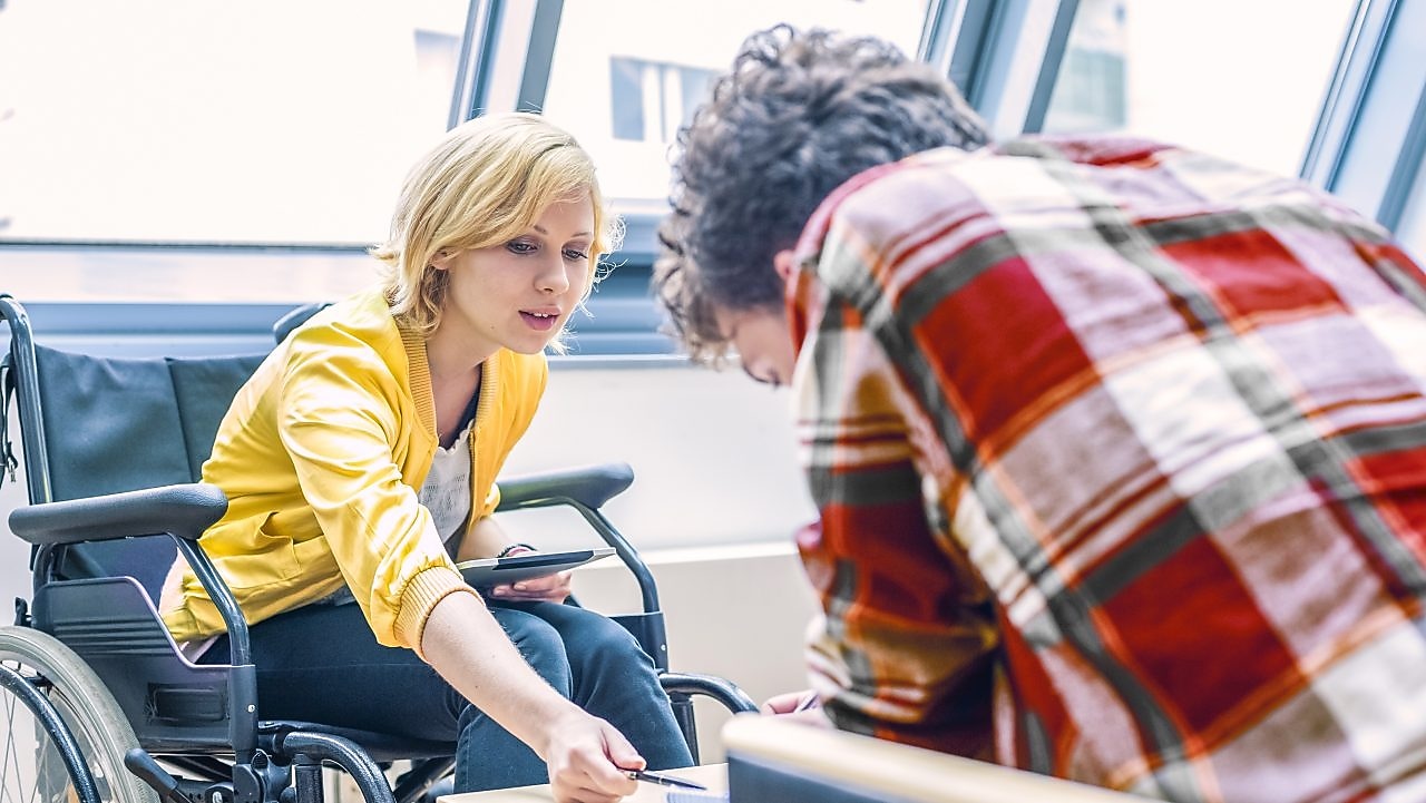 Tekerlekli sandalyeli bir kadın bir erkekle konuşuyor