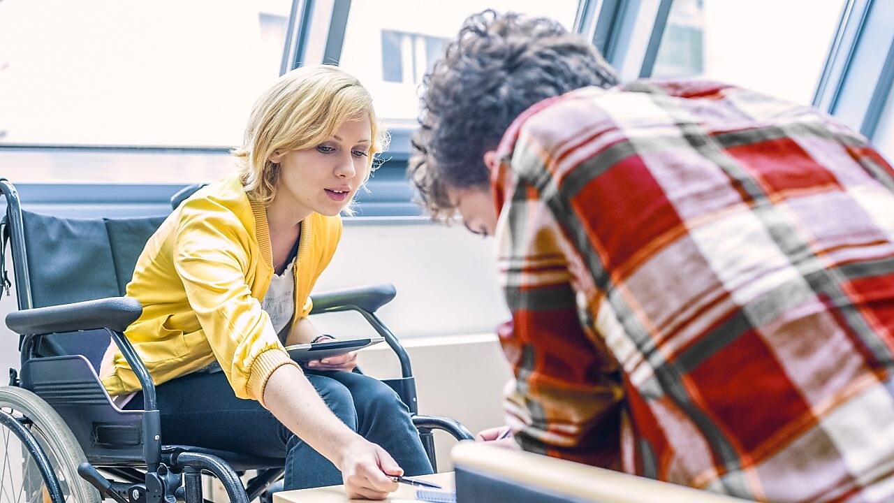 Tekerlekli sandalyeli bir kadın bir erkekle konuşuyor