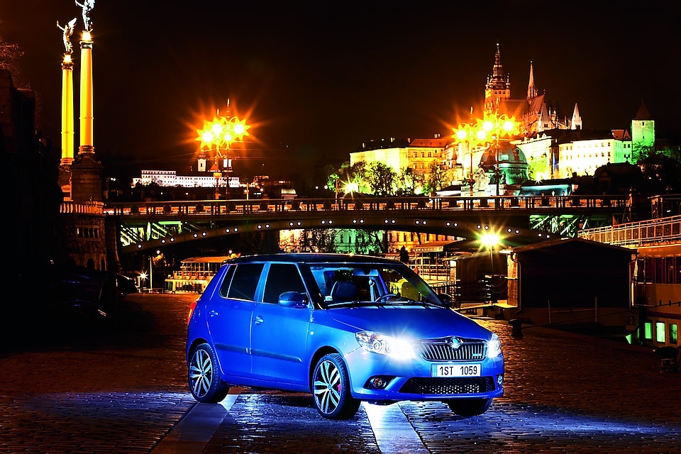 Gece Prag’da park halinde mavi bir otomobil, arka planda bir köprü ve kale