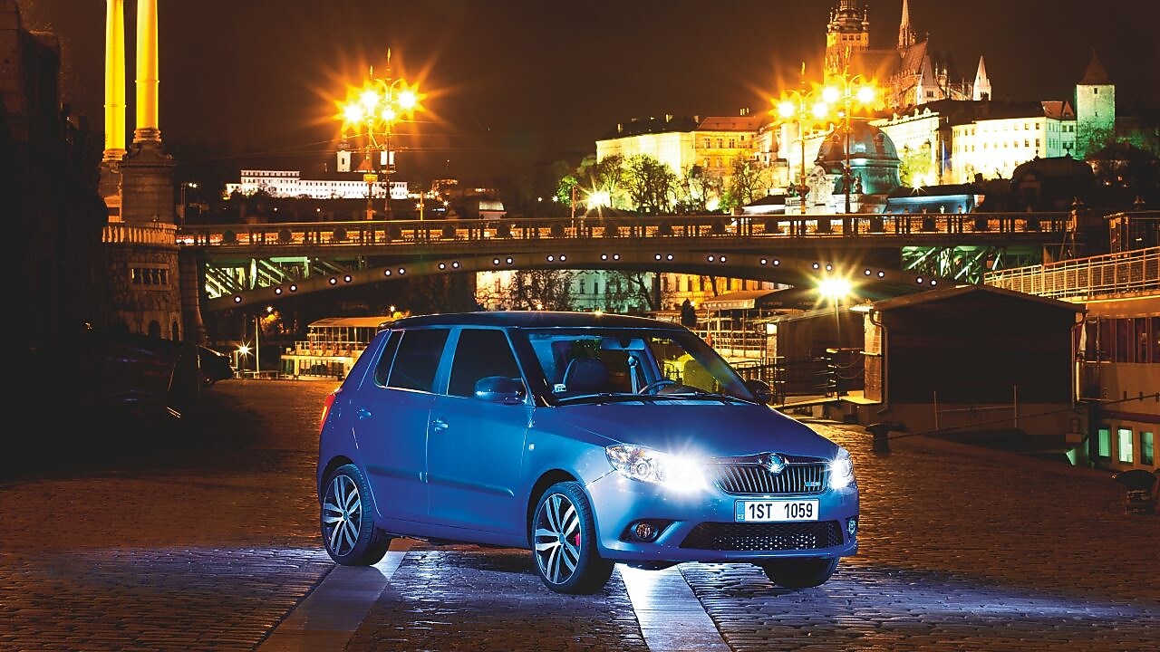 Gece Prag’da park halinde mavi bir otomobil, arka planda bir köprü ve kale