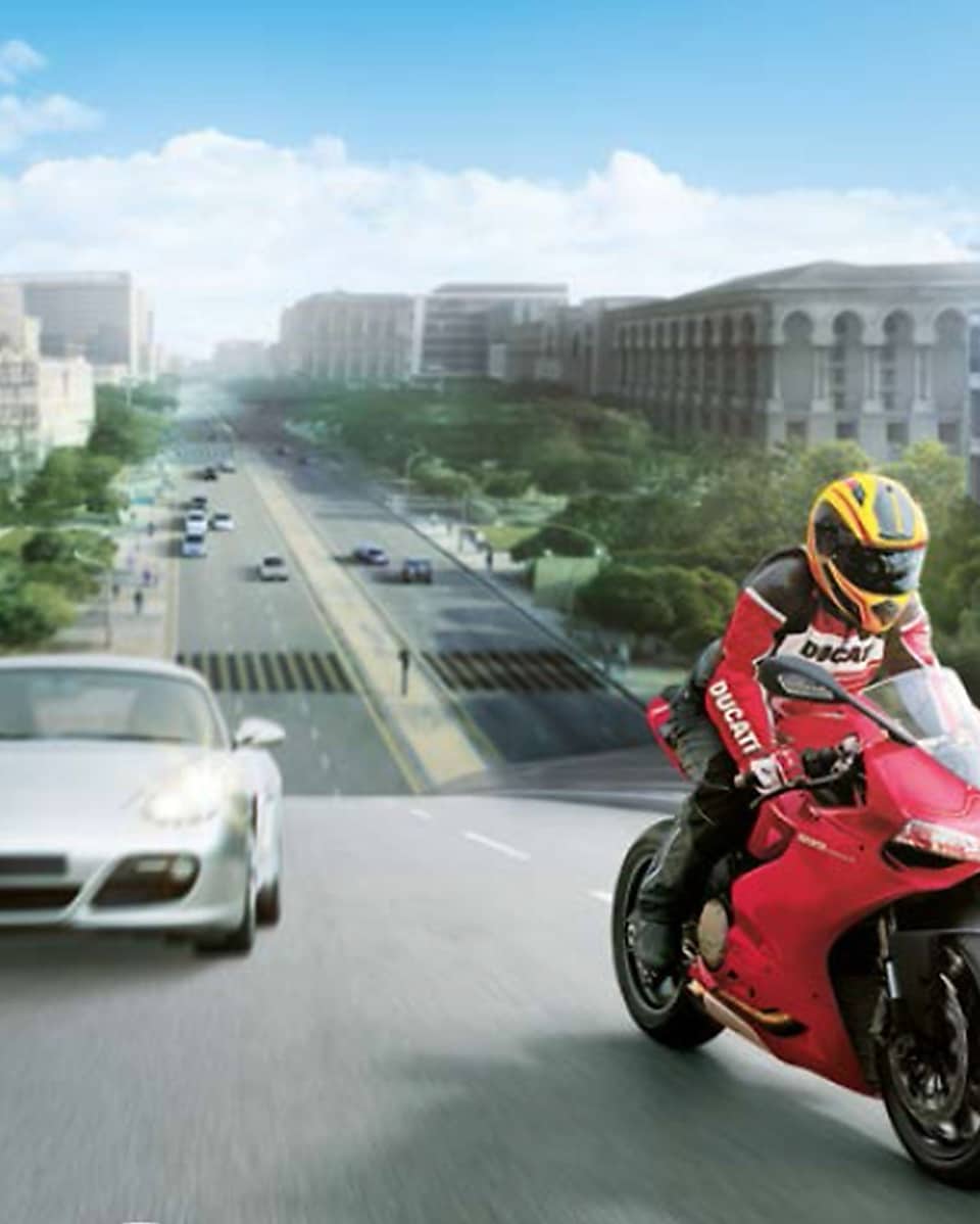 Arka planda otomobiller ve binalar olan yolda kırmızı motosiklet ve sürücü