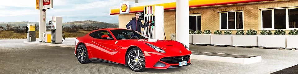 Kırmızı bir Ferrari bir Shell istasyonunda, bir adam benzin pompasına doğru eğiliyor