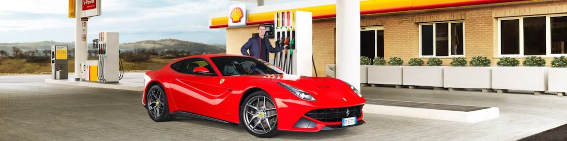 Kırmızı bir Ferrari bir Shell istasyonunda, bir adam benzin pompasına doğru eğiliyor